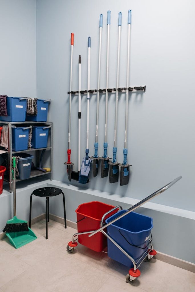 housekeeping-materials-used-for-cleaning-7108400 Neatly arranged cleaning tools in a storage room with mops, buckets, and shelving.